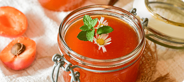 A jar of orange juice with a flower in it.