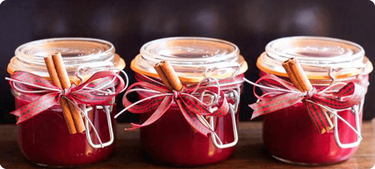 Three jars of jam with a cinnamon stick on top.