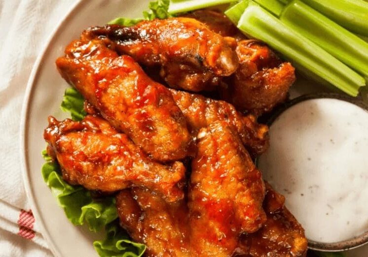 A plate of chicken wings with celery and sauce.